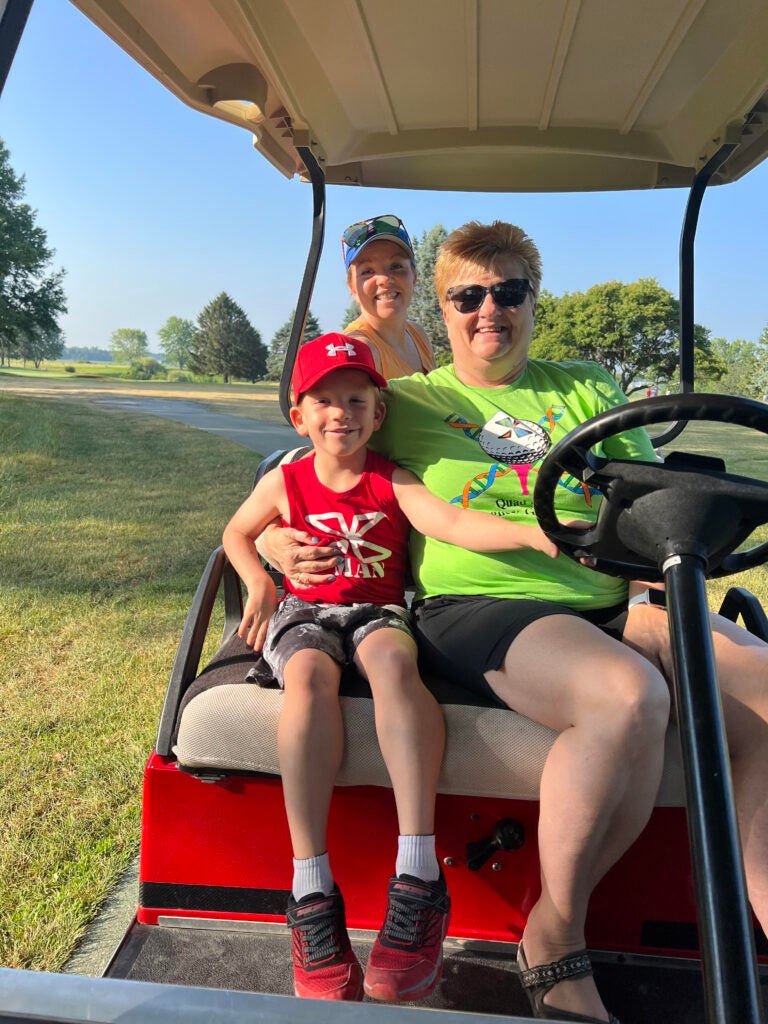 Grandma and grandsons riding in a gold cart.