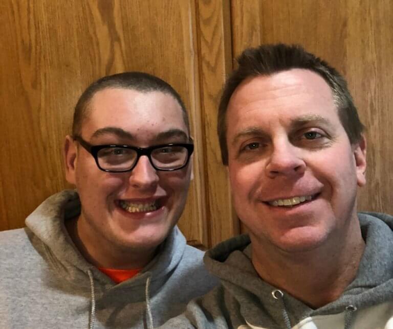 Cody and and his dad Garrett in front of a wood-paneled wall.