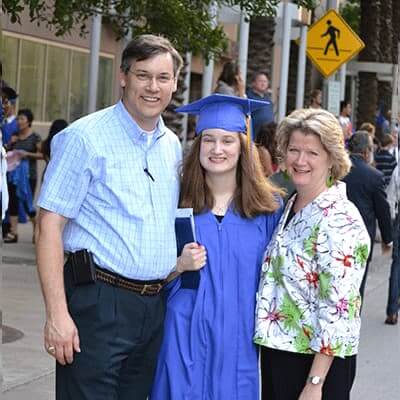 High school graduate in blue gown with mom and dad on graduation day