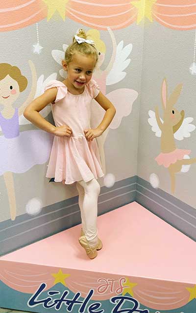 Gwynnie on a pink stage with angel backdrop and wearing a pink tutu, tights, and ballet shoes.