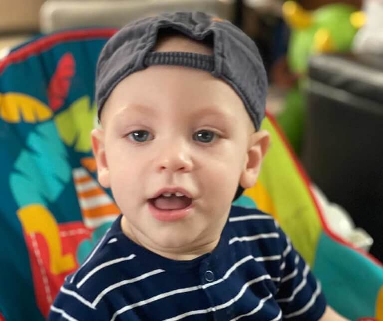 Harrison wearing a backwards baseball cap, blue and white striped t-shirt, and sitting in a colorful stroller.