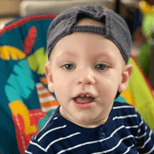 Male toddler wearing a blue and white striped t-shirt and baseball cap on backwards