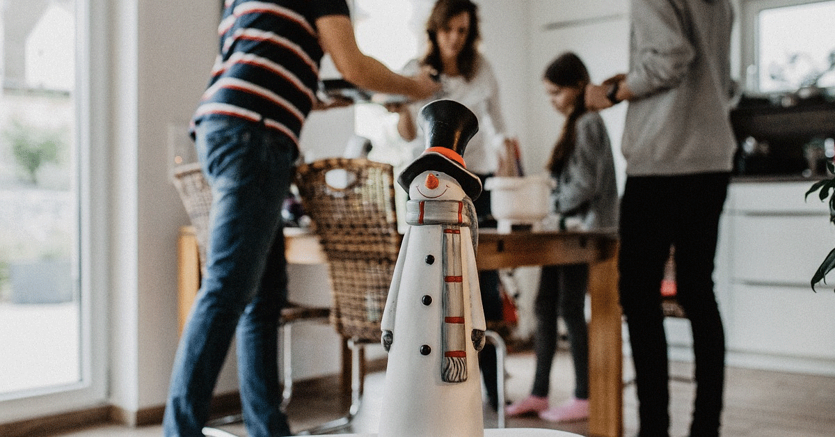 A snowman in the foreground of a family around a dining table.