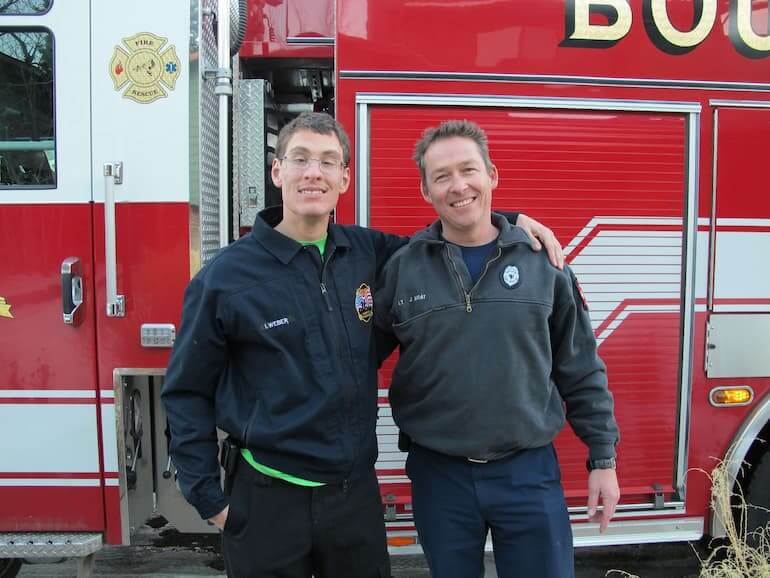 Ian and a firefighter standing in front of a fire truck