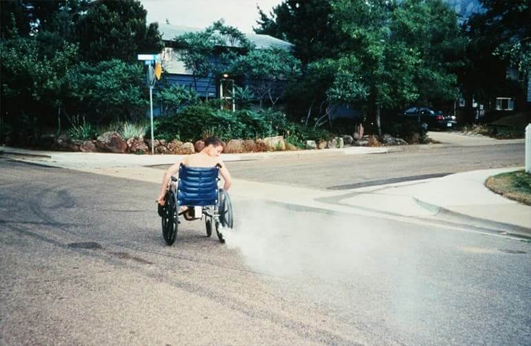 A boy in the street on a wheelchair with a smoking tail pipe.