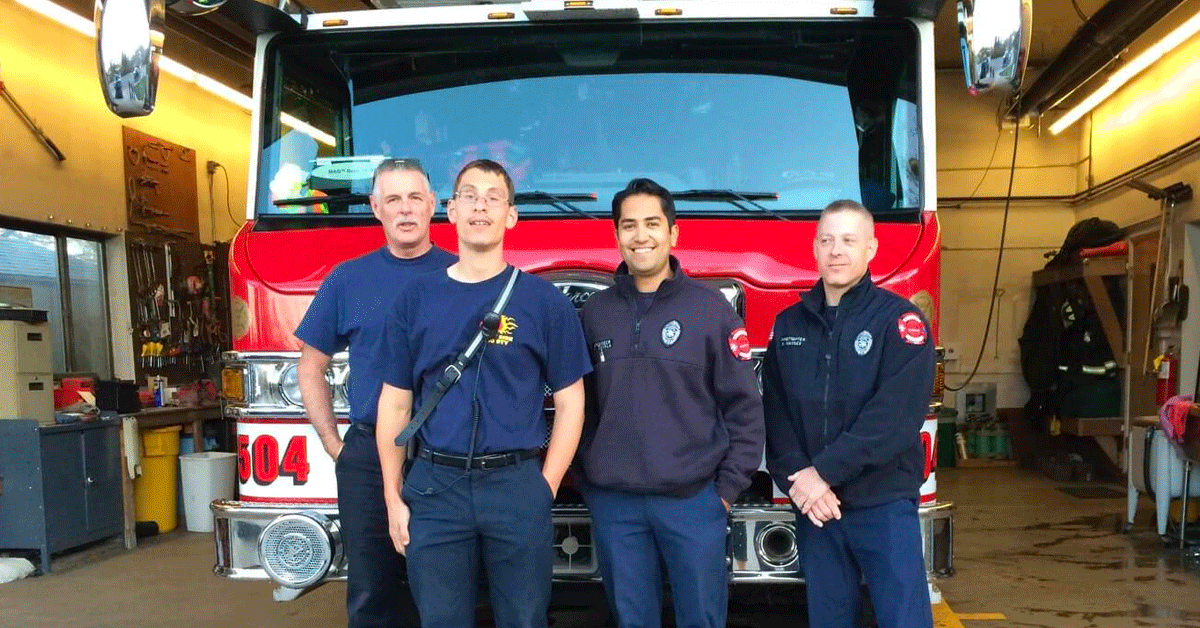 Ian with three members of the local fire station standing in front of a fire truck.