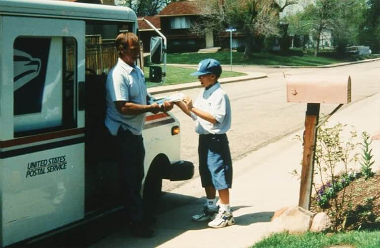 A boy helping a mailman by his truck