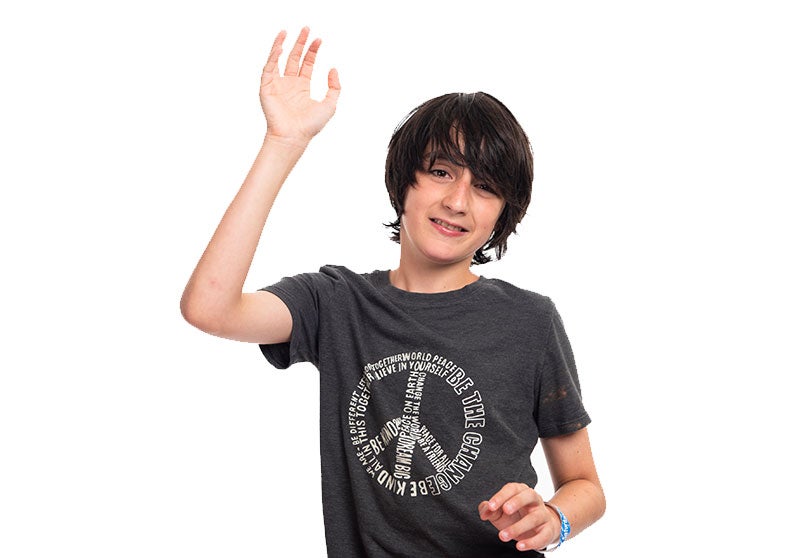 A young boy wearing a peace symbol t-shirt waving hello.