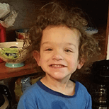 Male toddler with curly hair grinning with food on his face