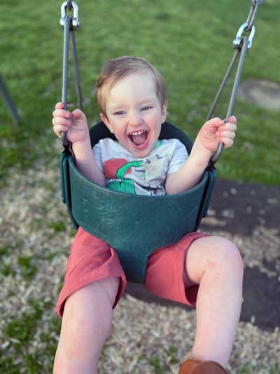 A young boy with Fragile X syndrome, Jack, laughing joyfully on an outdoor swing.