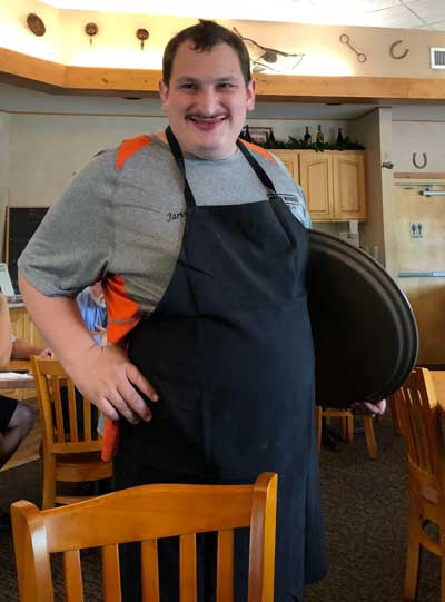 Jarvis, and adult with Fragile X syndrome, at work and wearing an apron and a happy smile.