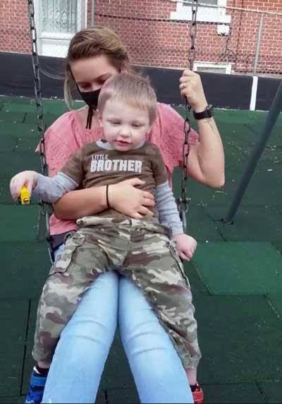 Jeriko, a young child with Fragile X syndrome, sitting on his mother's lap on a swing.