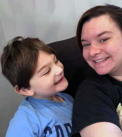 Laura with one of her young students, who has Fragile X syndrome, smiling at the camera.