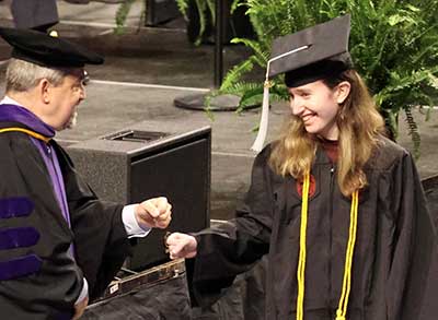 University of South Carolina Magna Cum Laude graduate Lauren Tiare Kuperman accepting her diploma, wearing graduation gown and four-sided hat.
