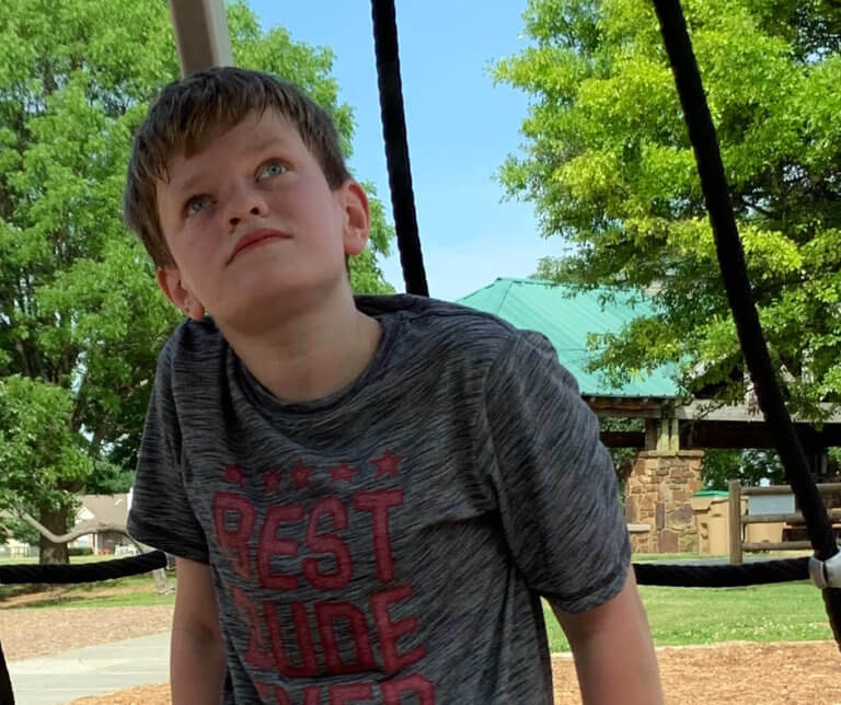 Leyton Stein sitting on a swingset gazing at the sky.