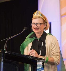 Linda Sorensen wearing a gold tiara addressing a crowd from a lecture stand.
