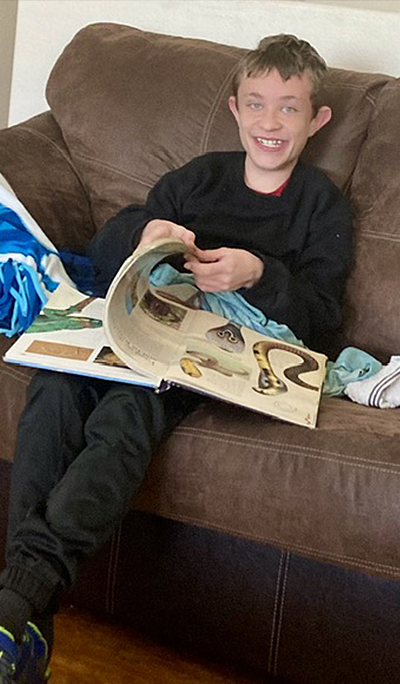 Mason Barnard reading a book while sitting on a couch at home.
