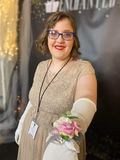 A beautiful young woman with Fragile X syndrome, Michelle, wearing an elegant lace gown, elbow-length white gloves, and a pink wrist corsage.