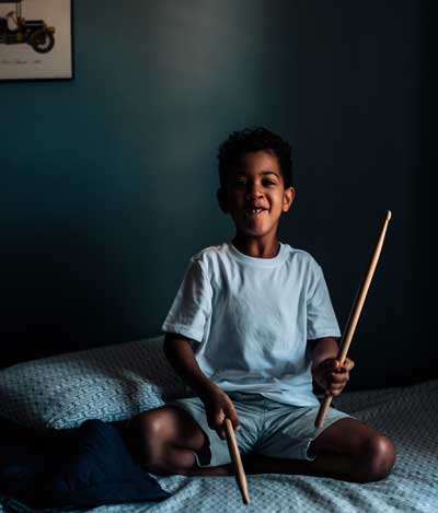 A young boy, Noah, sitting on his bed and playing air drums.