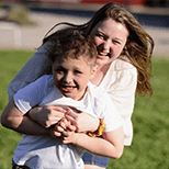 A teen girl holding and playing with a young boy outdoors and laughing