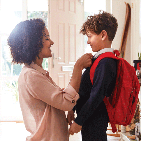 A mom kneeling on the floor fixing a young boy's tie.