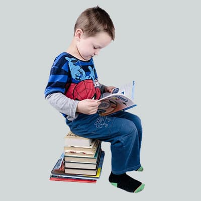 Young boy sitting on stack of books while reading