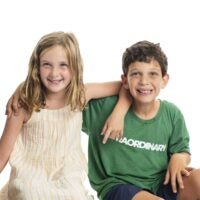 A young girl in a dress and her brother in a green t-shirt, sitting side-by-side.