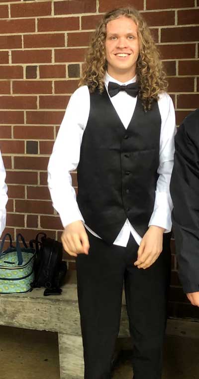 A young man with Fragile X syndrome, William "Willie" Gregory, wearing a white dress shirt and tuxedo pants, vest, and bow tie, blonde curls and a winning smile.