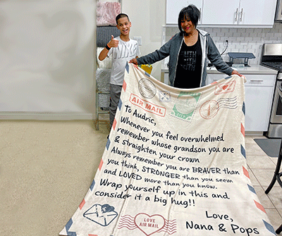 Barbara Newsome in her kitchen with her grandson showing off a large blanket with a printed letter to her grandson