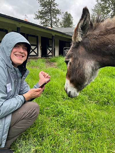 A young boy Zack Griffin outdoors on a farm in a field of green grass petting a donkey.